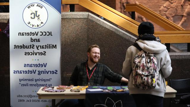 Student representating the veteran and military resource center is at a table speaking to another student.